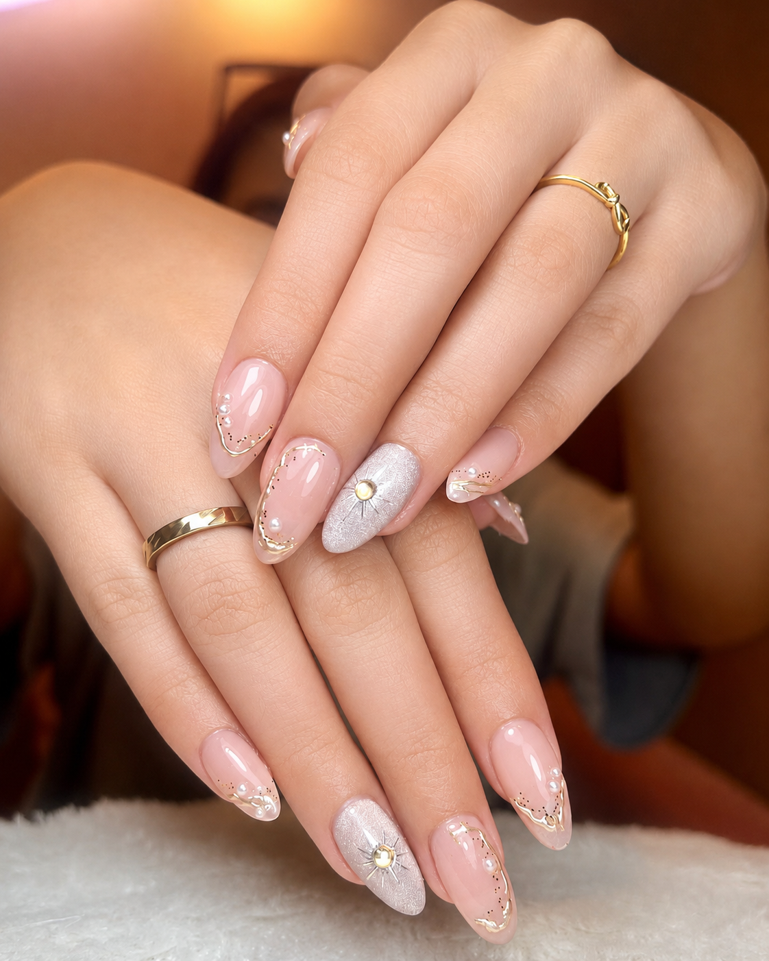 Close-up of pale pink almond nails with delicate white and gold floral details.
